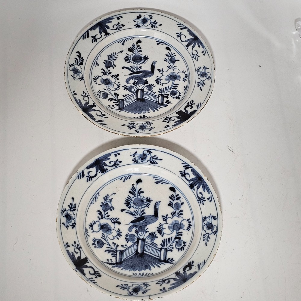 A pair of round antique Delft ceramic plates featuring hand-painted blue and white bird and floral motifs on a white tin-glazed background.
