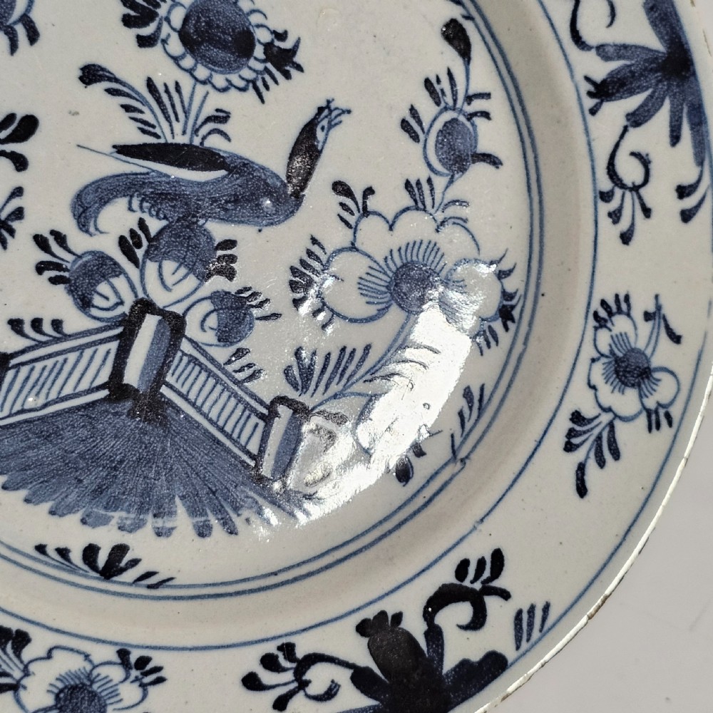 A pair of round antique Delft ceramic plates featuring hand-painted blue and white bird and floral motifs on a white tin-glazed background. View V