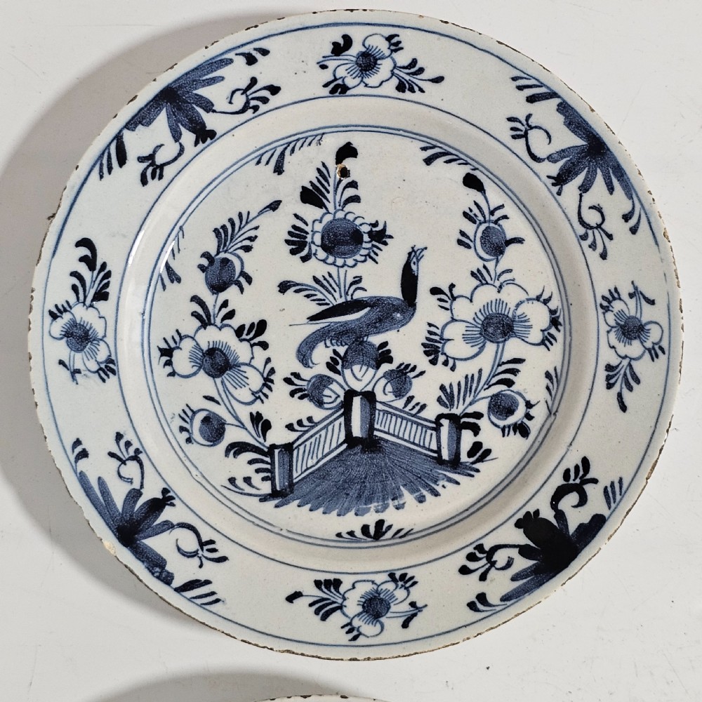 A pair of round antique Delft ceramic plates featuring hand-painted blue and white bird and floral motifs on a white tin-glazed background. View X