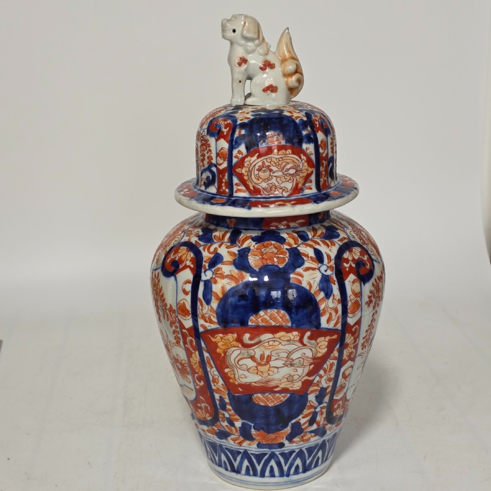 A 19th-century Japanese Imari porcelain covered jar decorated with cobalt blue and rust red floral panel motifs, topped with a sculpted foo dog finial lid.