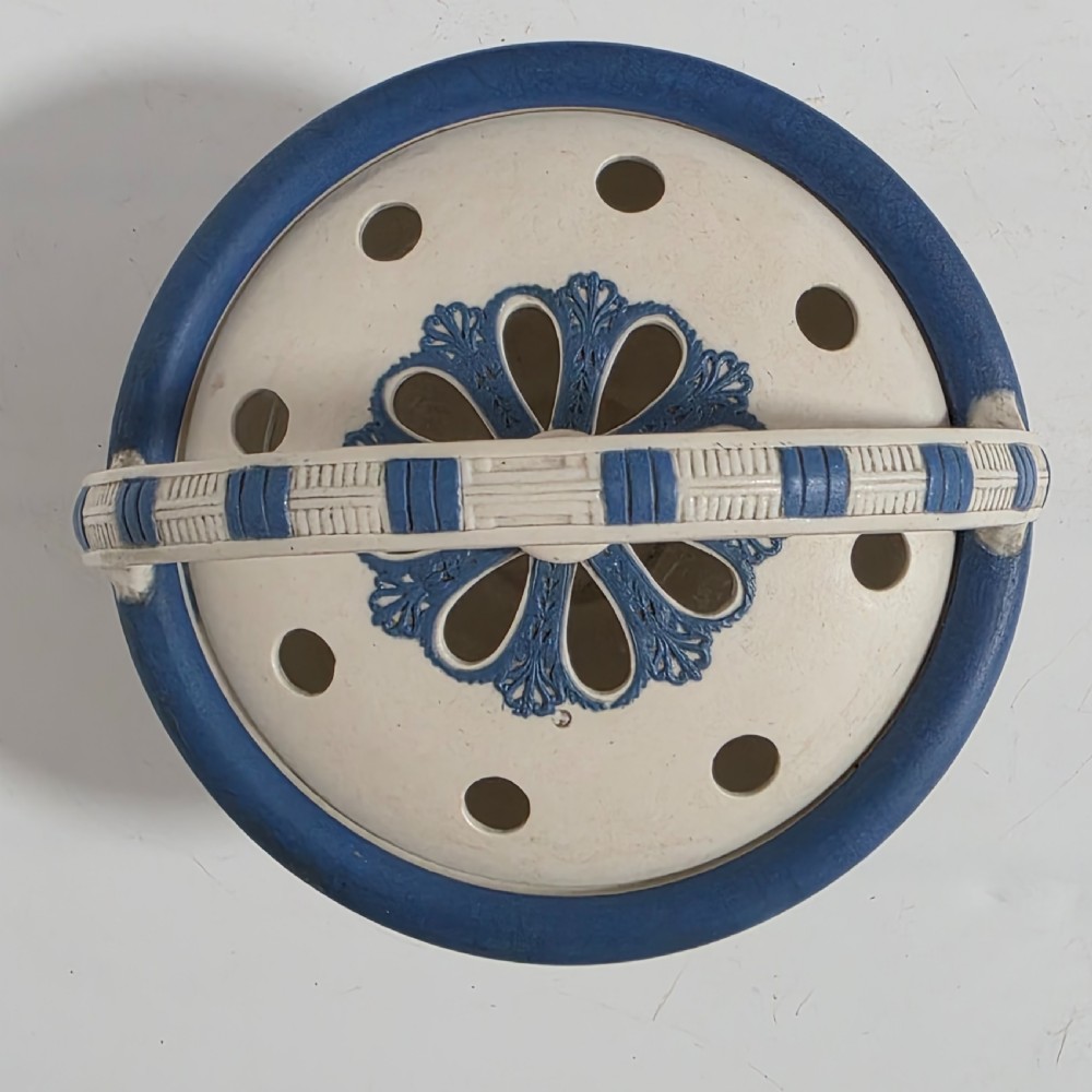 An off-white Georgian stoneware pot pourri basket featuring an overhead handle, pierced cover, and cobalt blue applied grapevine sprig decoration. View II