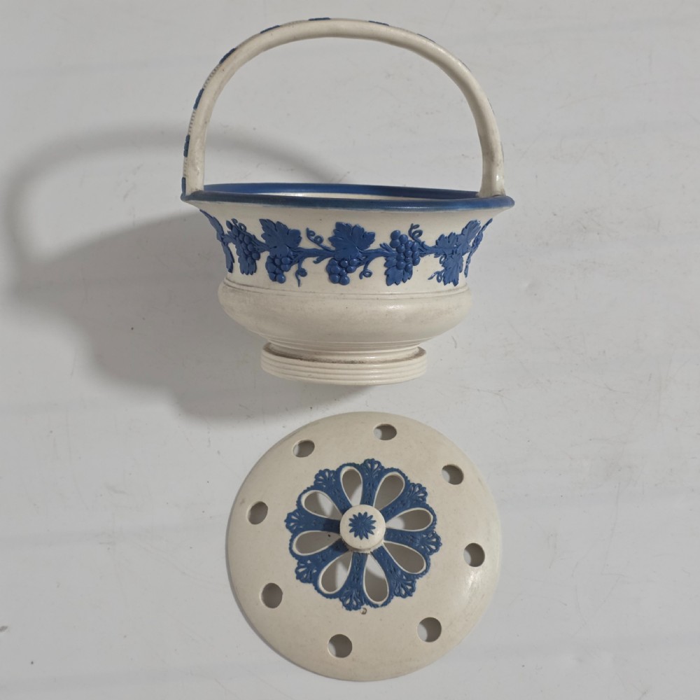 An off-white Georgian stoneware pot pourri basket featuring an overhead handle, pierced cover, and cobalt blue applied grapevine sprig decoration. View III