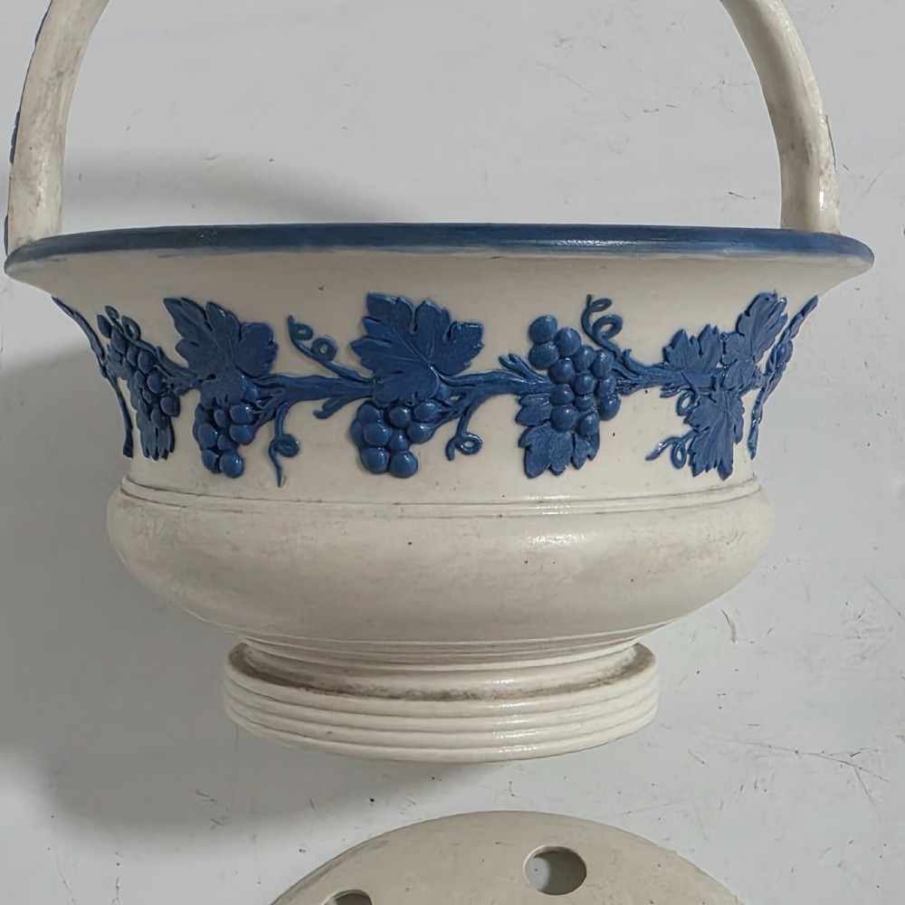 An off-white Georgian stoneware pot pourri basket featuring an overhead handle, pierced cover, and cobalt blue applied grapevine sprig decoration. View VII