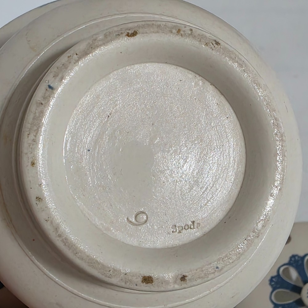 An off-white Georgian stoneware pot pourri basket featuring an overhead handle, pierced cover, and cobalt blue applied grapevine sprig decoration. View IX