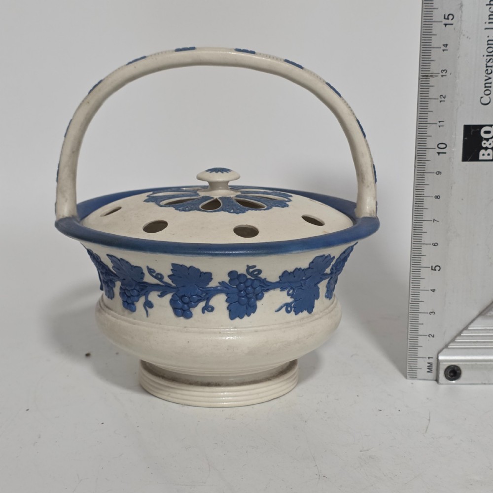 An off-white Georgian stoneware pot pourri basket featuring an overhead handle, pierced cover, and cobalt blue applied grapevine sprig decoration. View XI