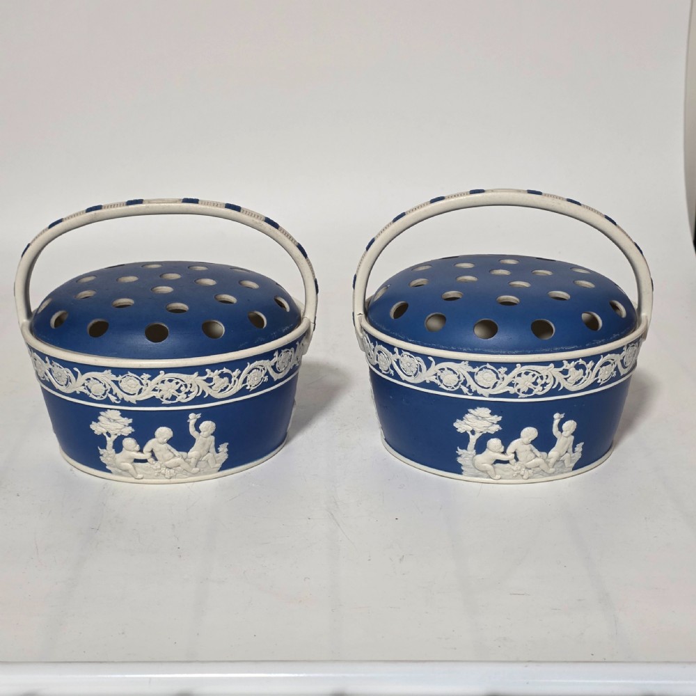 A pair of blue and white Georgian ceramic pot pourri baskets with pierced lids, white classical cherub reliefs, and overhead handles.