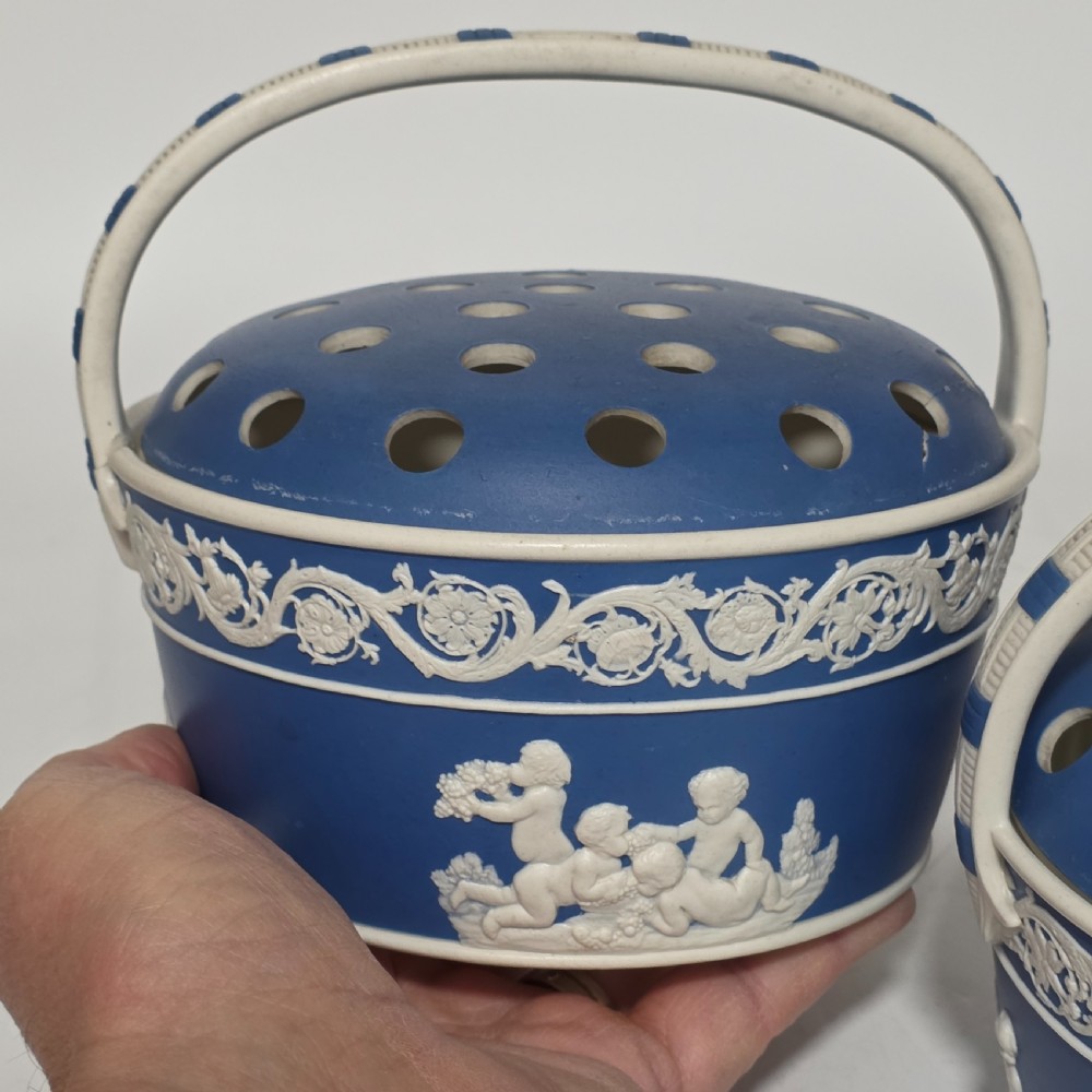 A pair of blue and white Georgian ceramic pot pourri baskets with pierced lids, white classical cherub reliefs, and overhead handles. View V