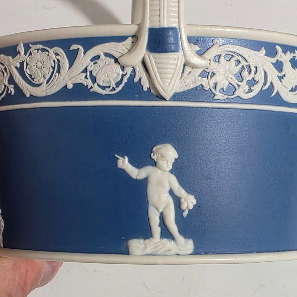 A pair of blue and white Georgian ceramic pot pourri baskets with pierced lids, white classical cherub reliefs, and overhead handles. View XX