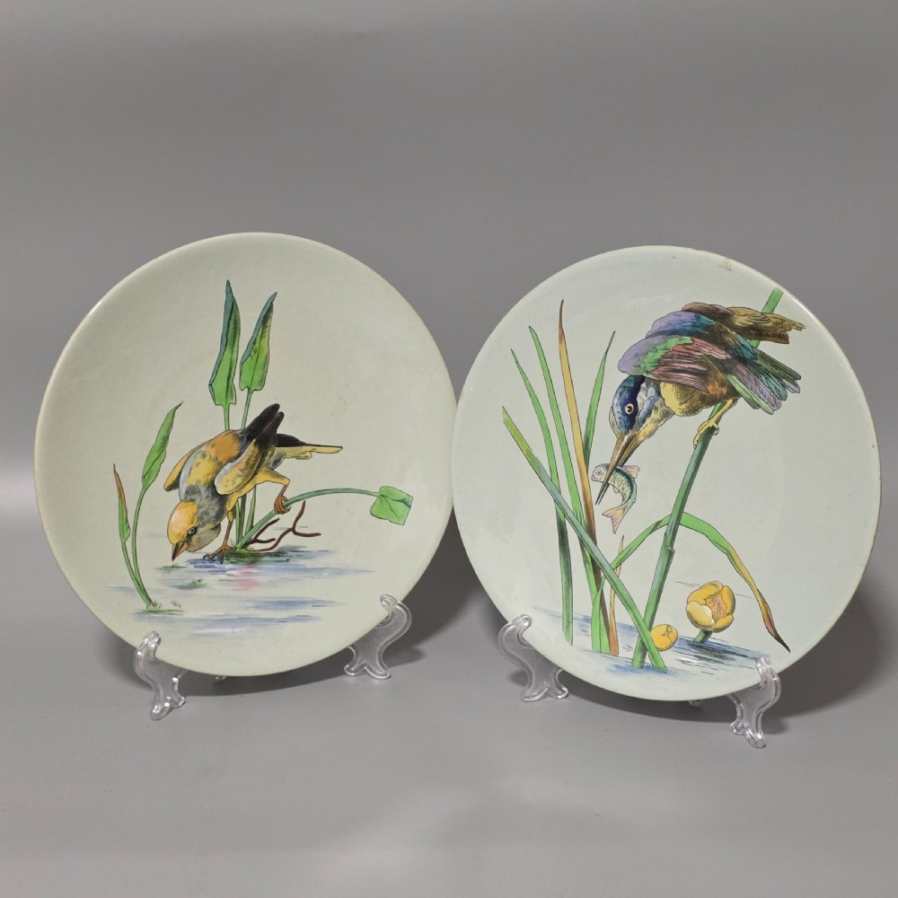A pair of circular pale green ceramic display plates hand painted with detailed birds near water lilies and reeds.