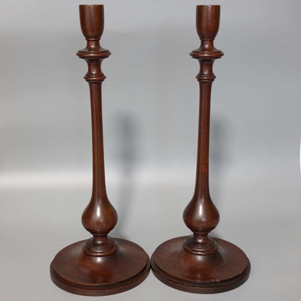 A pair of tall turned dark wood candlesticks featuring bulbous lower shafts and circular stepped bases.