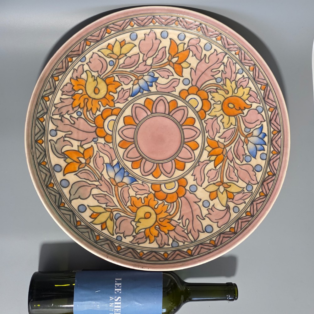 A circular Art Deco earthenware charger decorated with pink, orange, yellow, and blue stylised floral tubelined motifs. View III