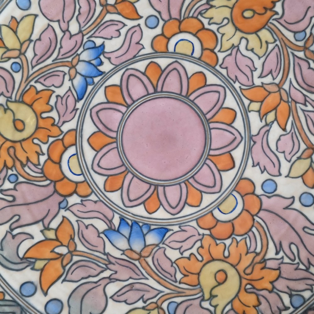 A circular Art Deco earthenware charger decorated with pink, orange, yellow, and blue stylised floral tubelined motifs. View IV