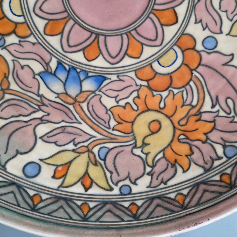 A circular Art Deco earthenware charger decorated with pink, orange, yellow, and blue stylised floral tubelined motifs. View V