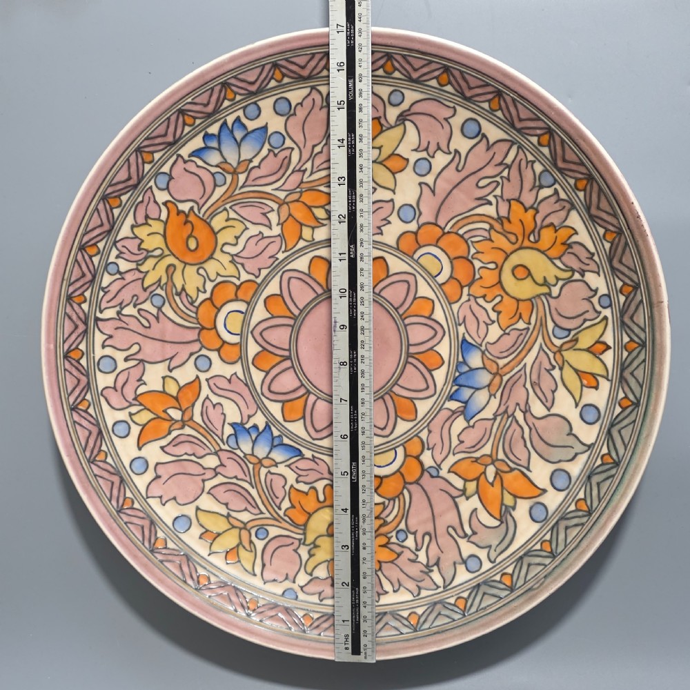 A circular Art Deco earthenware charger decorated with pink, orange, yellow, and blue stylised floral tubelined motifs. View VI