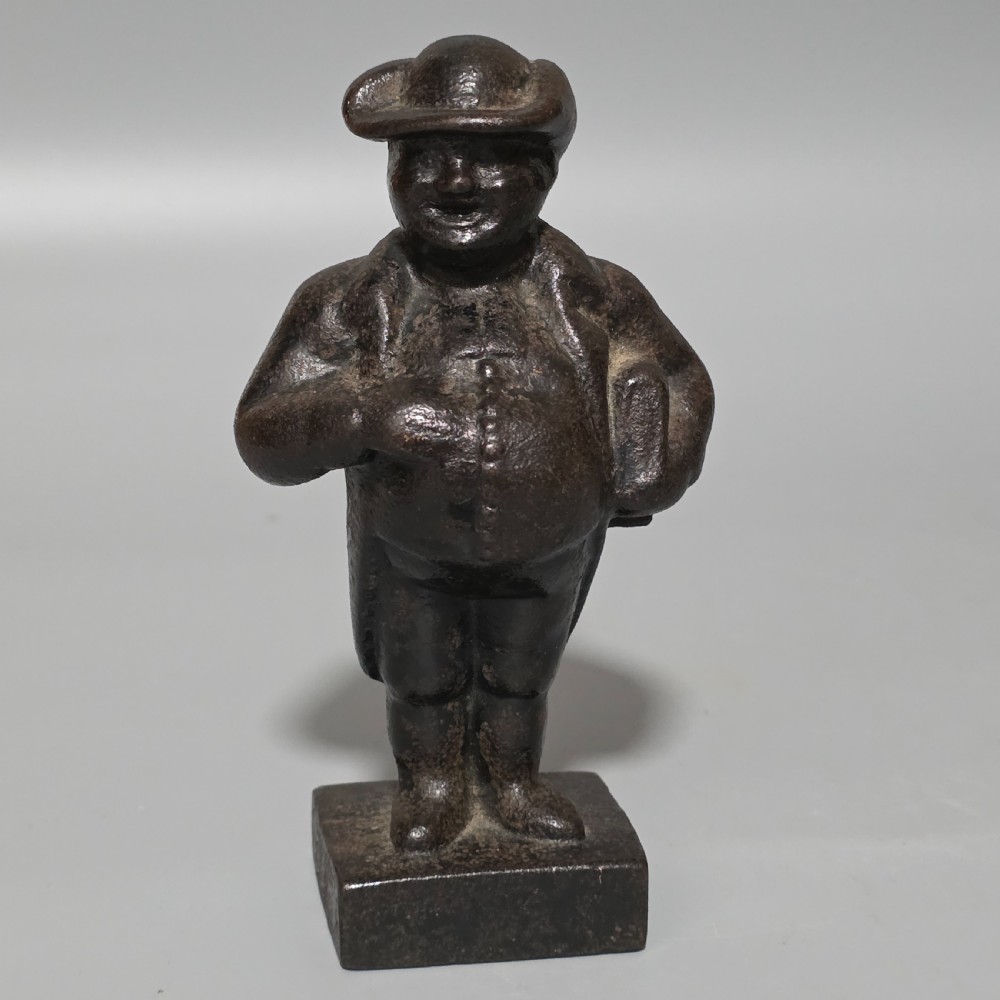 A dark cast iron paperweight depicting a standing nineteenth-century gentleman on a square plinth base.
