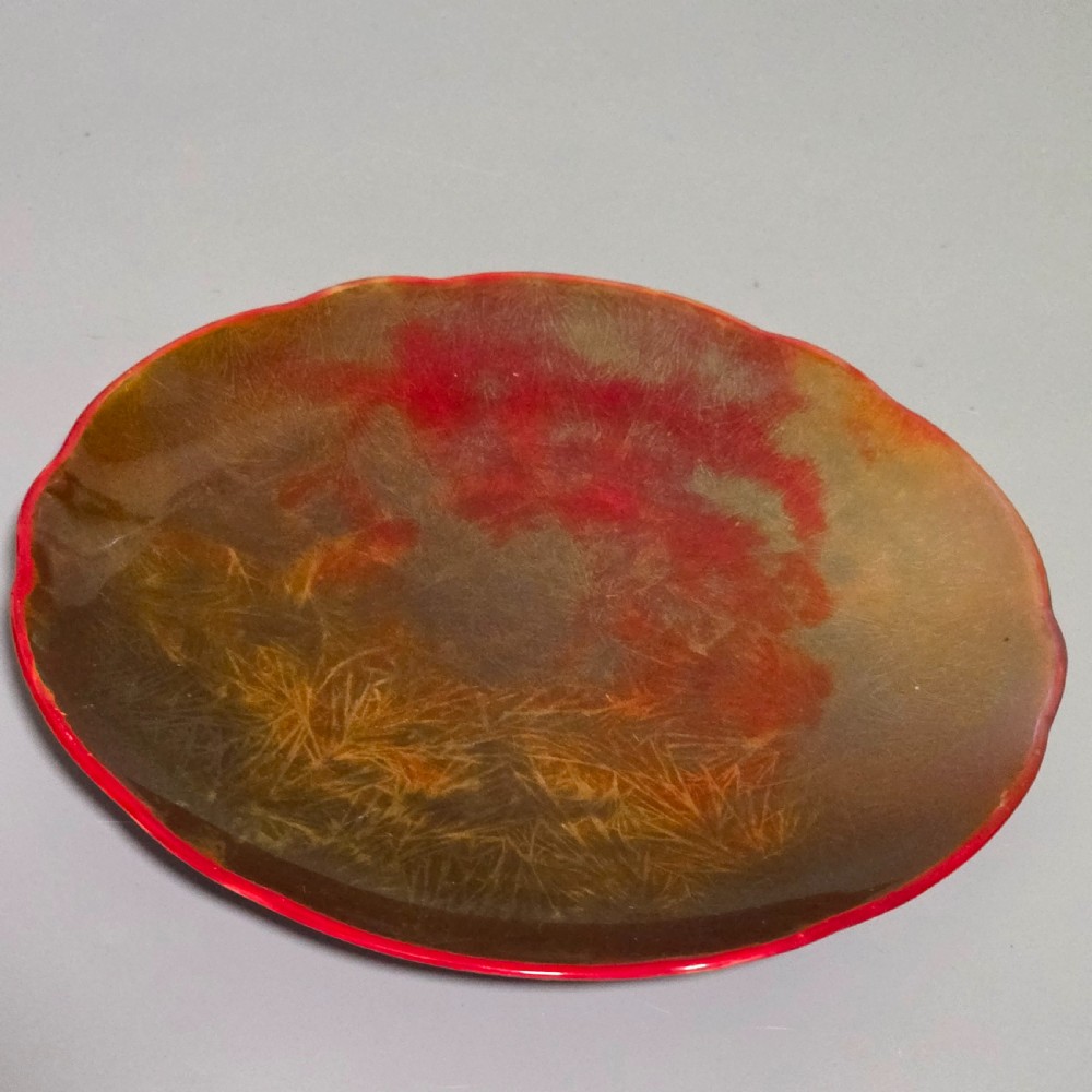 A shallow ceramic art pottery plate featuring a crimson red flambe glaze combined with golden-brown crystalline textures and a scalloped edge.