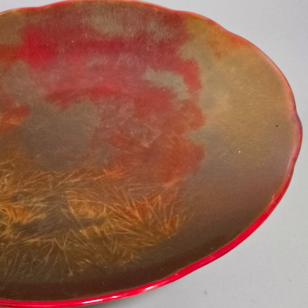 A shallow ceramic art pottery plate featuring a crimson red flambe glaze combined with golden-brown crystalline textures and a scalloped edge. View II
