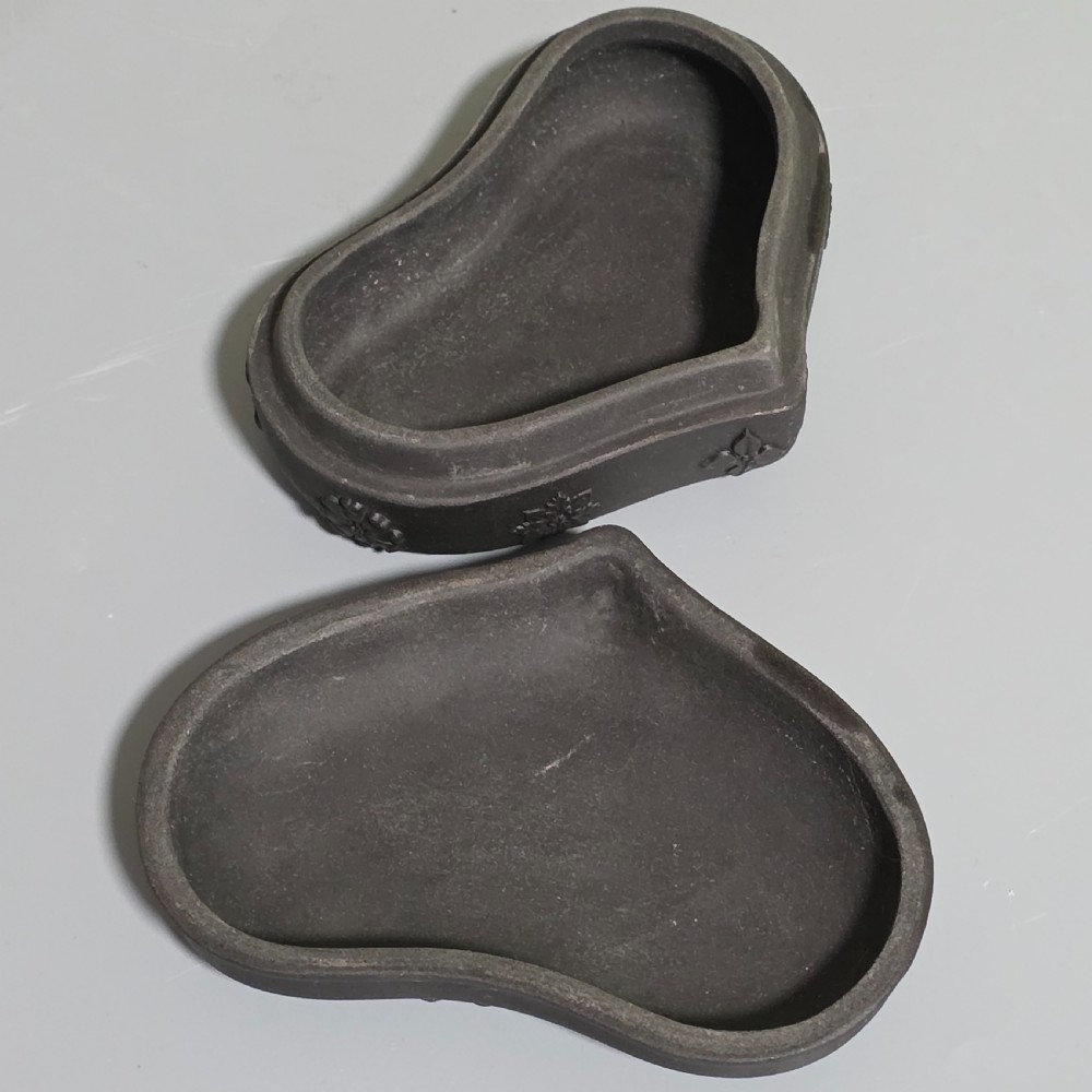 A kidney-shaped matte black basalt stoneware trinket box featuring Neoclassical relief figures, rosettes, and floral garland borders. View IX