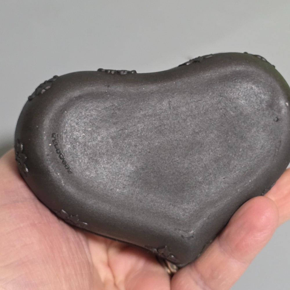 A kidney-shaped matte black basalt stoneware trinket box featuring Neoclassical relief figures, rosettes, and floral garland borders. View X