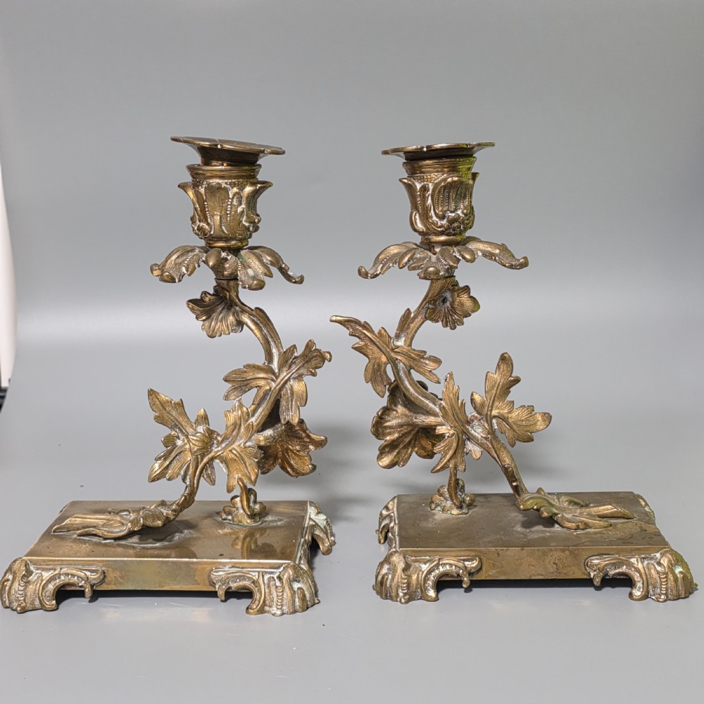 A pair of 19th-century French Napoleon III cast brass candlesticks featuring ornate scrolling leaf motifs and rectangular bases.