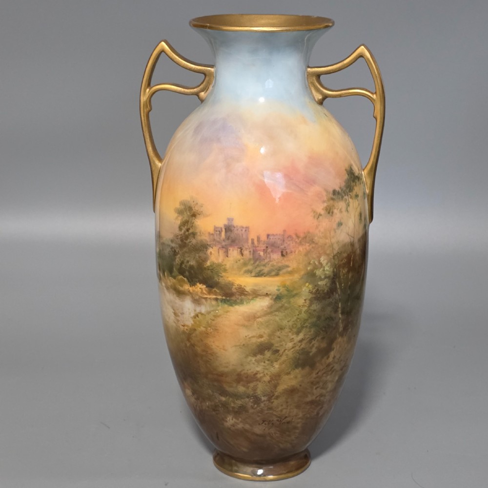A tall porcelain vase featuring twin gilded handles and a handpainted landscape scene depicting Windsor Castle against a soft sunset sky.