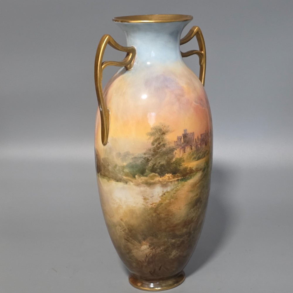 A tall porcelain vase featuring twin gilded handles and a handpainted landscape scene depicting Windsor Castle against a soft sunset sky. View II