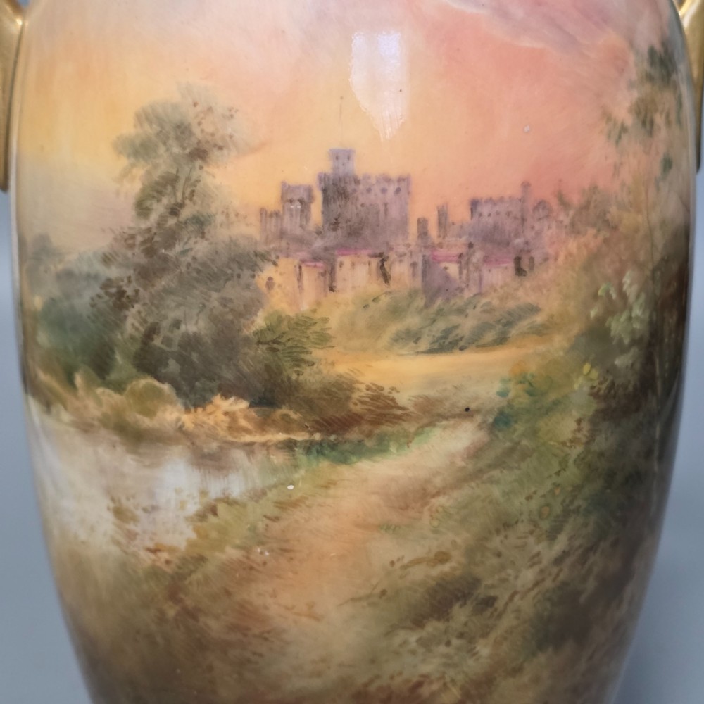 A tall porcelain vase featuring twin gilded handles and a handpainted landscape scene depicting Windsor Castle against a soft sunset sky. View VII
