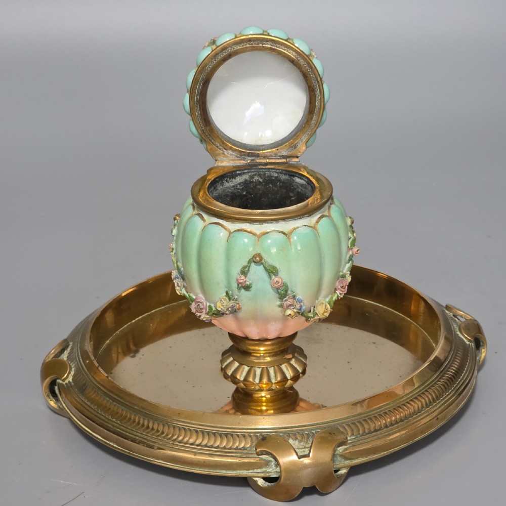A fluted pastel green and pink porcelain inkwell decorated with applied floral swags, mounted on a turned brass pedestal within a circular brass tray base. View II