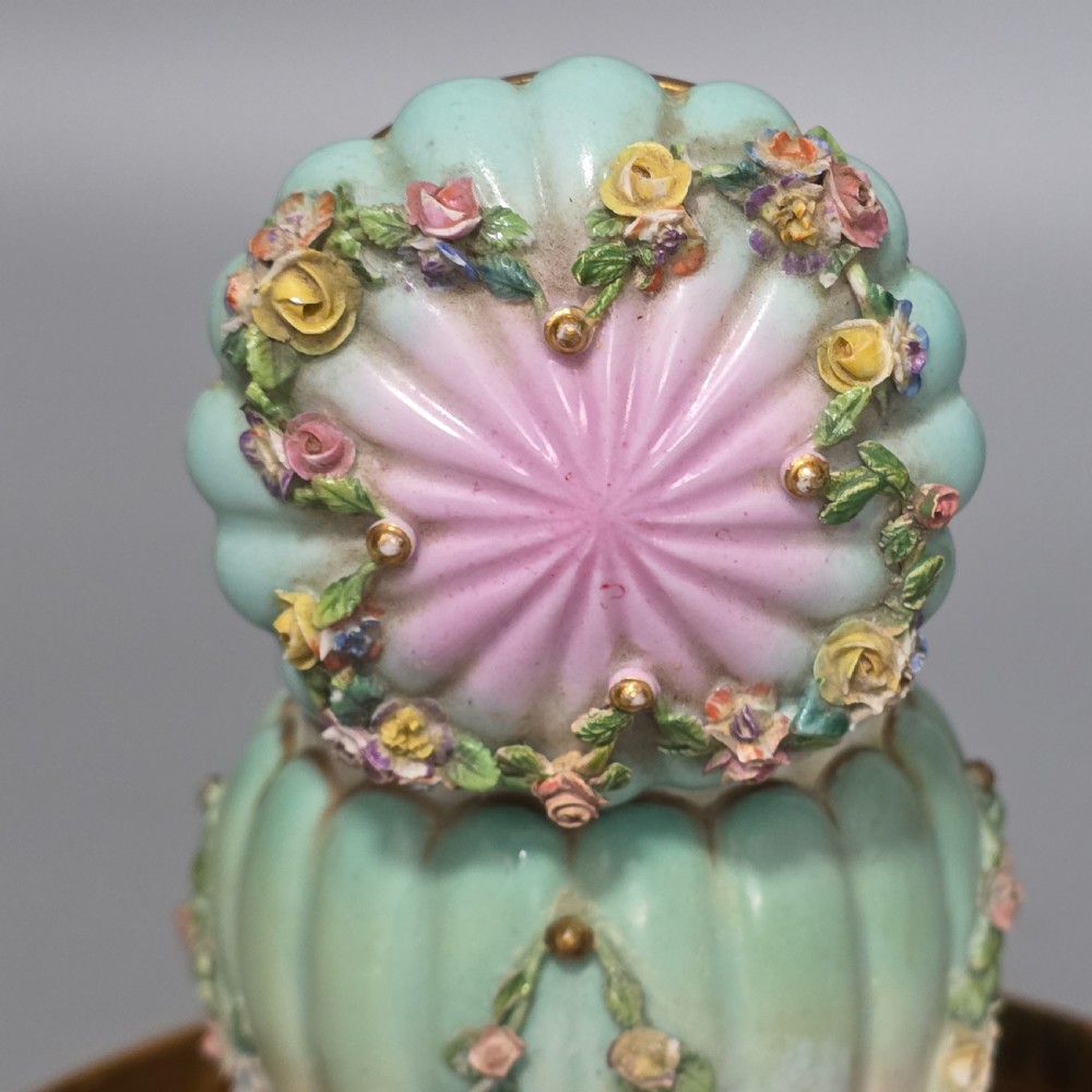 A fluted pastel green and pink porcelain inkwell decorated with applied floral swags, mounted on a turned brass pedestal within a circular brass tray base. View V