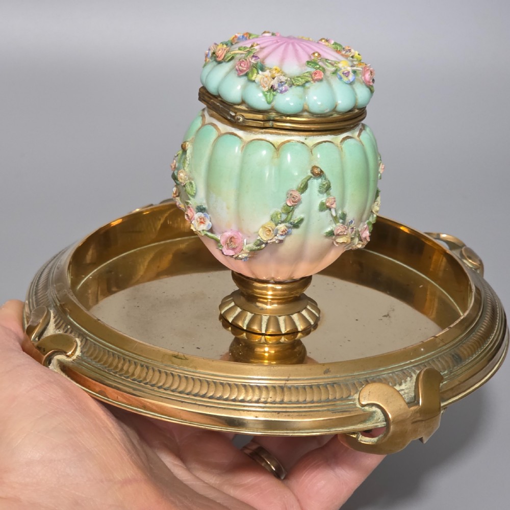 A fluted pastel green and pink porcelain inkwell decorated with applied floral swags, mounted on a turned brass pedestal within a circular brass tray base. View IX