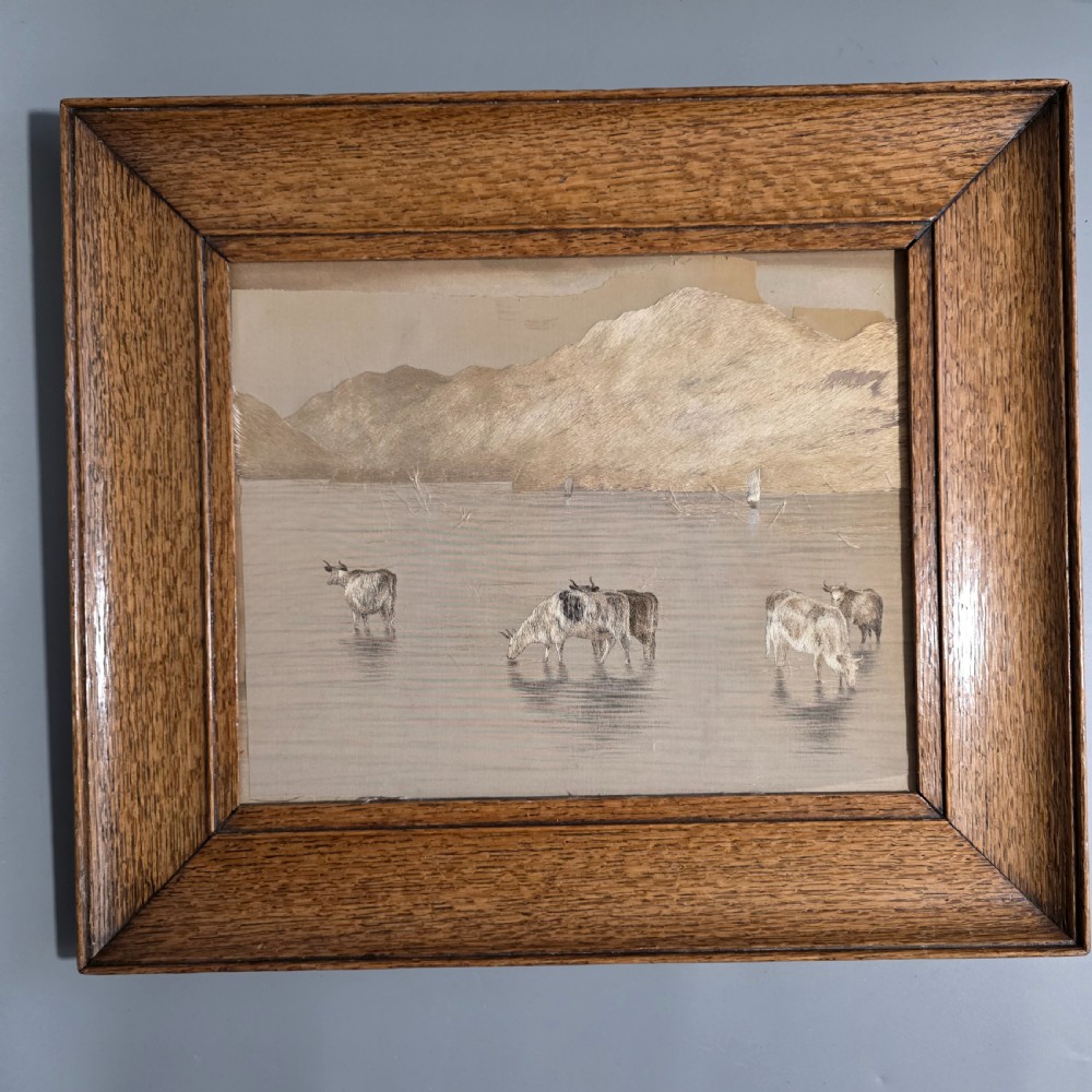 A framed Chinese silk embroidery panel depicting cattle standing in water in front of a mountainous background, presented in a wide oak frame.