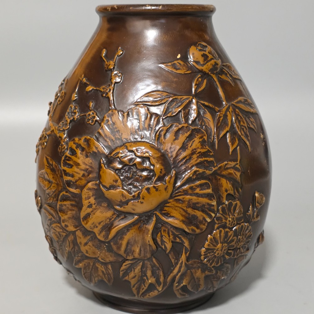A dark brown patinated bronze vase featuring raised high-relief floral carvings of large peonies and chrysanthemums.