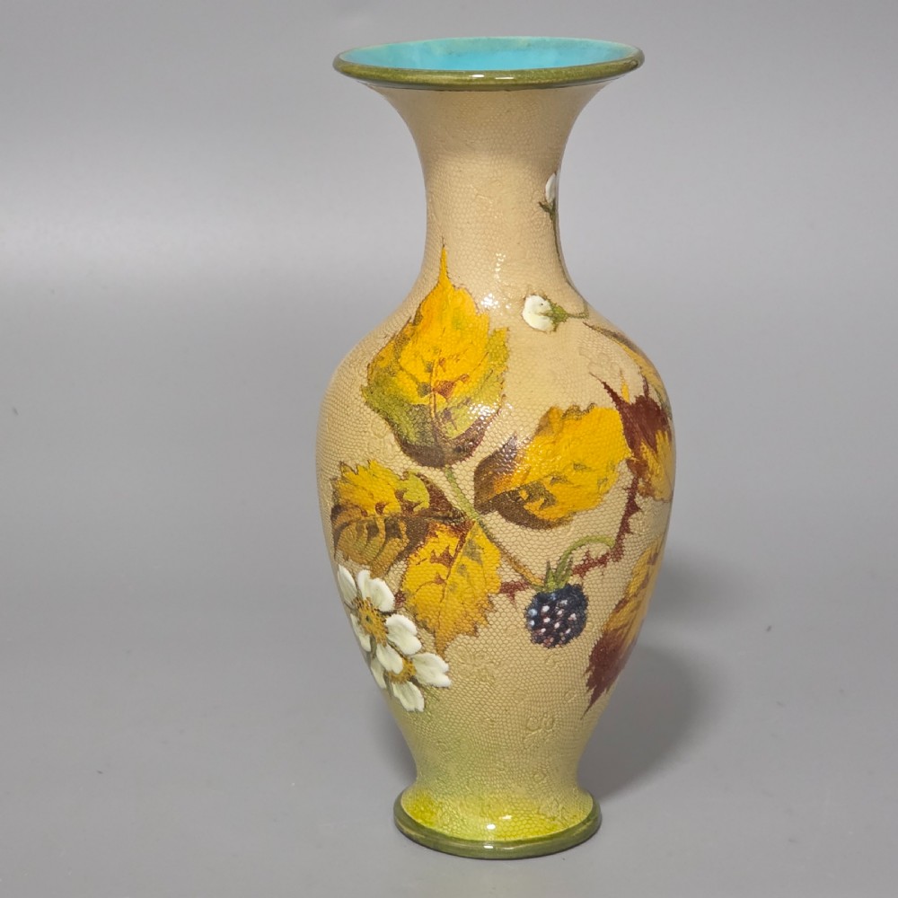 A baluster-shaped Doulton Lambeth ceramic vase featuring a textured lace-patterned buff background painted with botanical autumn leaves and blackberries, finished with a bright turquoise interior rim.