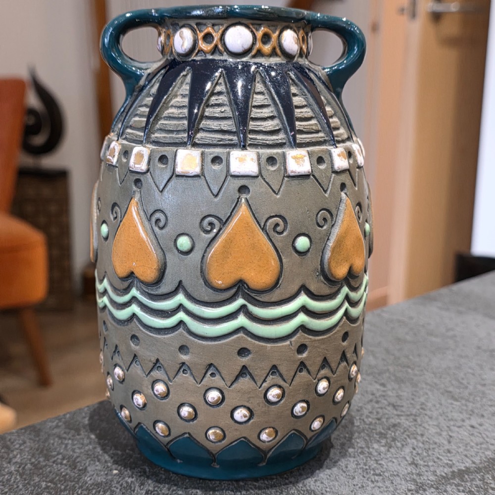 An Art Deco ceramic amphora vase featuring two green handles, raised geometric patterns, heart-shaped motifs, and a glazed teal, grey, and ochre colour scheme. View III