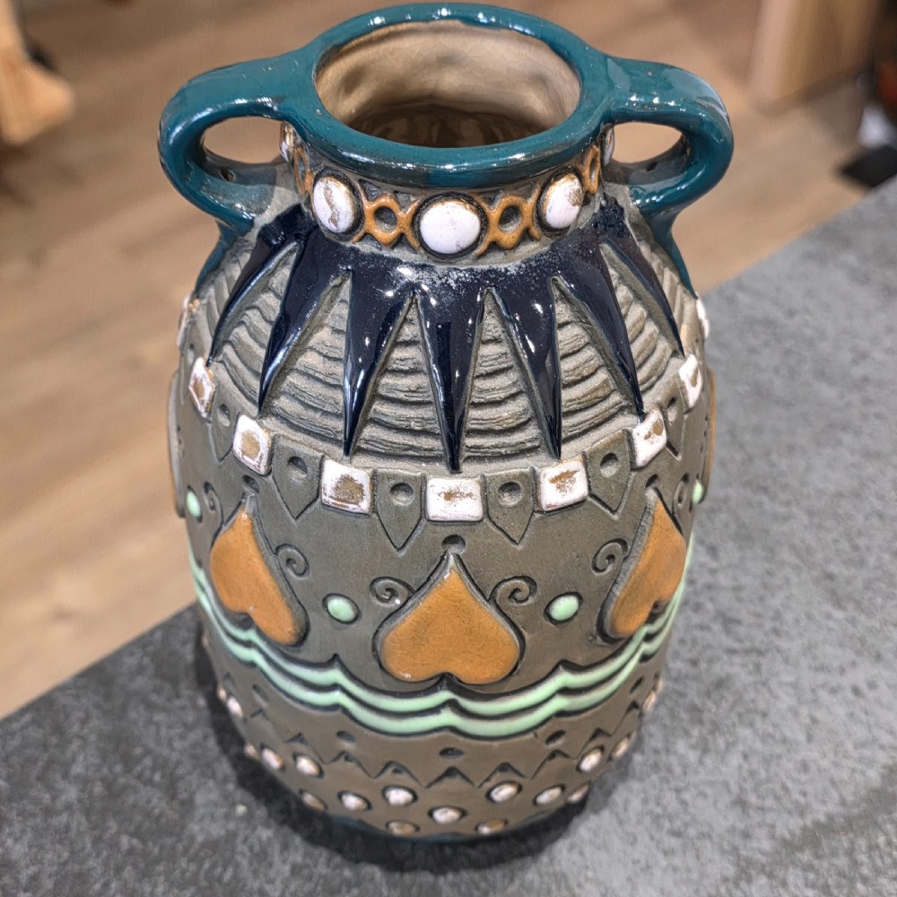An Art Deco ceramic amphora vase featuring two green handles, raised geometric patterns, heart-shaped motifs, and a glazed teal, grey, and ochre colour scheme. View IV