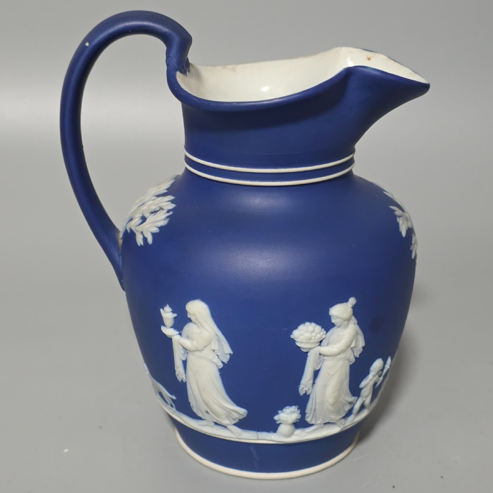 A cobalt blue stoneware jug featuring white raised neoclassical figures in relief with a high arched handle and curved spout. View III