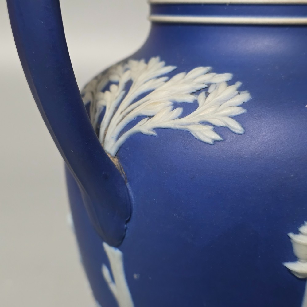 A cobalt blue stoneware jug featuring white raised neoclassical figures in relief with a high arched handle and curved spout. View IX