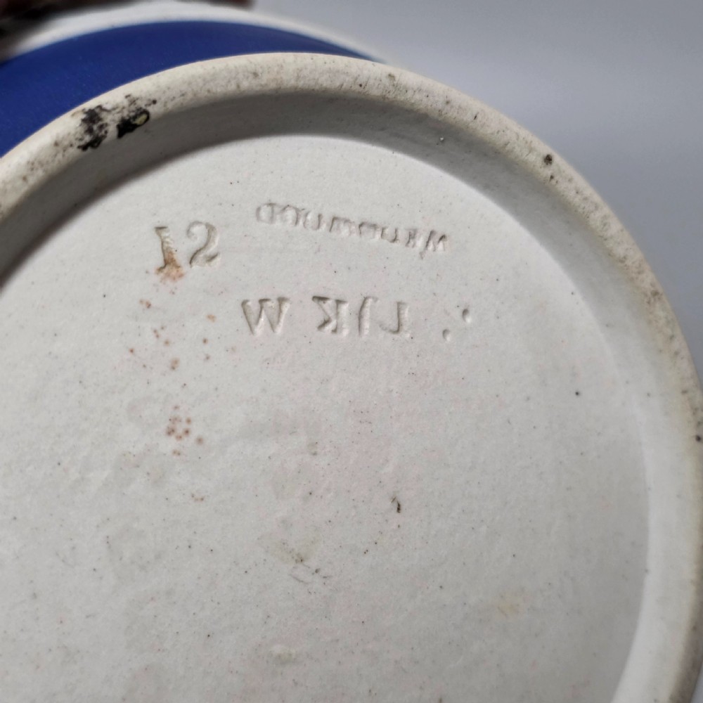 A cobalt blue stoneware jug featuring white raised neoclassical figures in relief with a high arched handle and curved spout. View XII