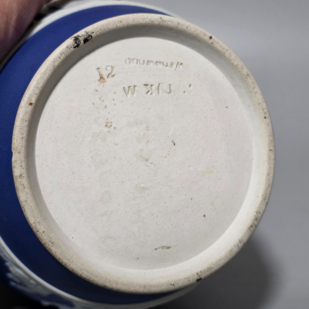 A cobalt blue stoneware jug featuring white raised neoclassical figures in relief with a high arched handle and curved spout. View XIII