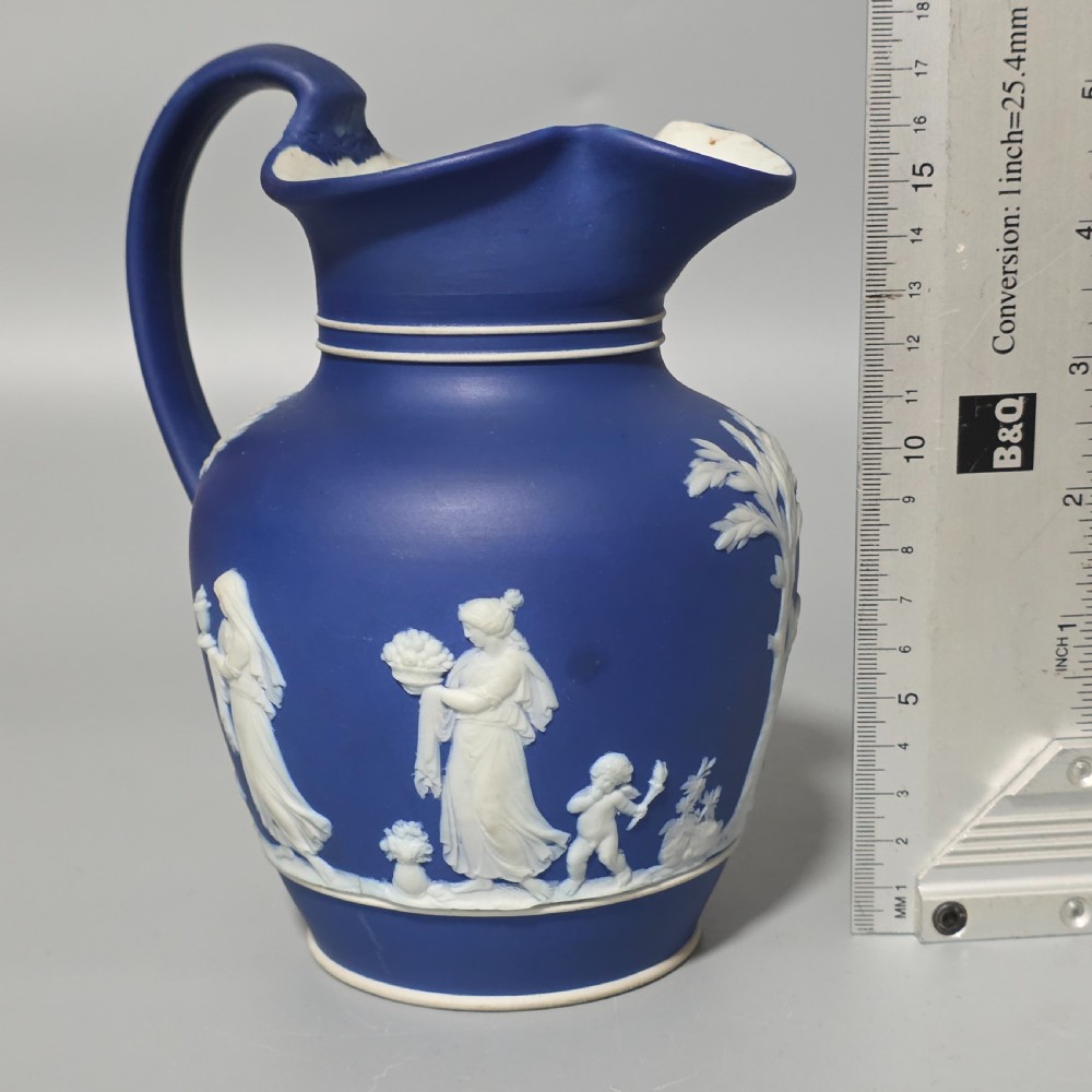 A cobalt blue stoneware jug featuring white raised neoclassical figures in relief with a high arched handle and curved spout. View XV