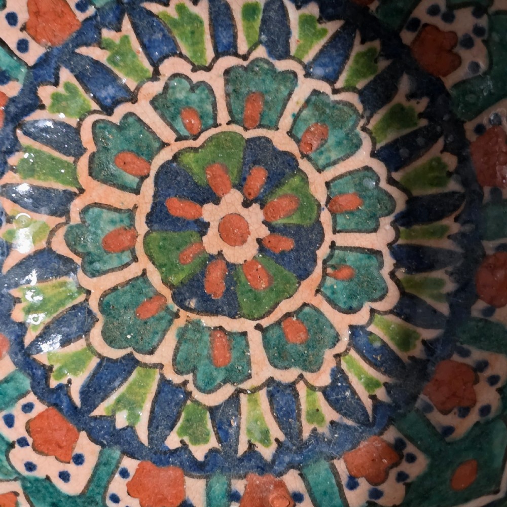 A circular hand-painted antique Middle Eastern ceramic bowl decorated with turquoise, cobalt blue, and terracotta geometric motifs. View II