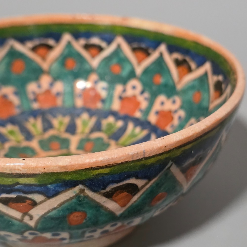 A circular hand-painted antique Middle Eastern ceramic bowl decorated with turquoise, cobalt blue, and terracotta geometric motifs. View III
