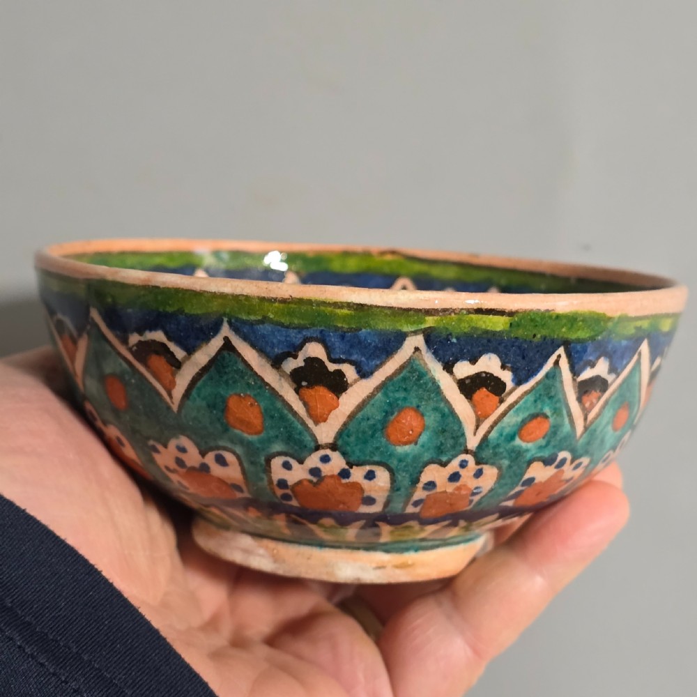 A circular hand-painted antique Middle Eastern ceramic bowl decorated with turquoise, cobalt blue, and terracotta geometric motifs. View VII