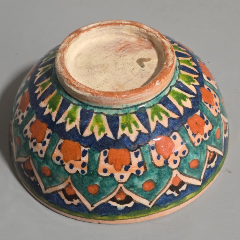 A circular hand-painted antique Middle Eastern ceramic bowl decorated with turquoise, cobalt blue, and terracotta geometric motifs. View IX