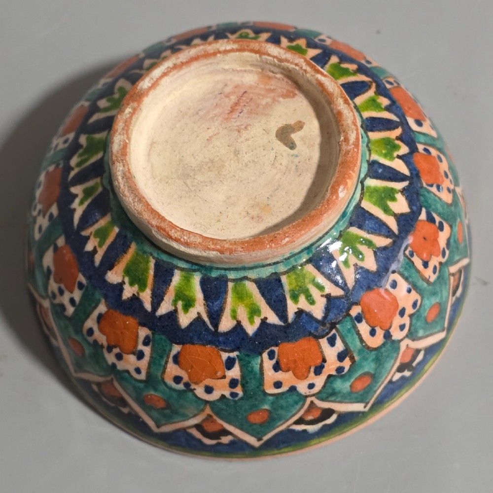A circular hand-painted antique Middle Eastern ceramic bowl decorated with turquoise, cobalt blue, and terracotta geometric motifs. View X