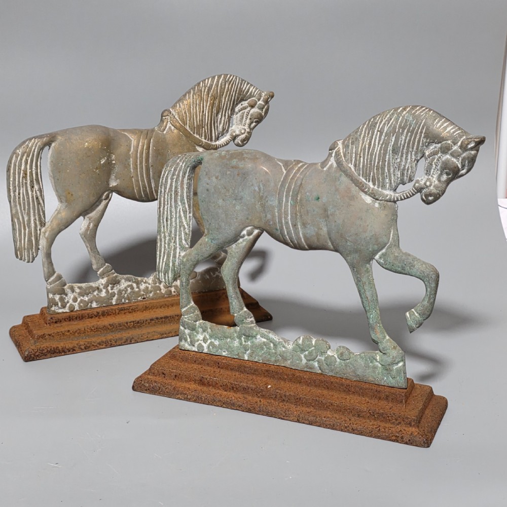 A pair of 19th-century cast iron and brass doorstops featuring prancing horses mounted on stepped rectangular bases with aged patina.
