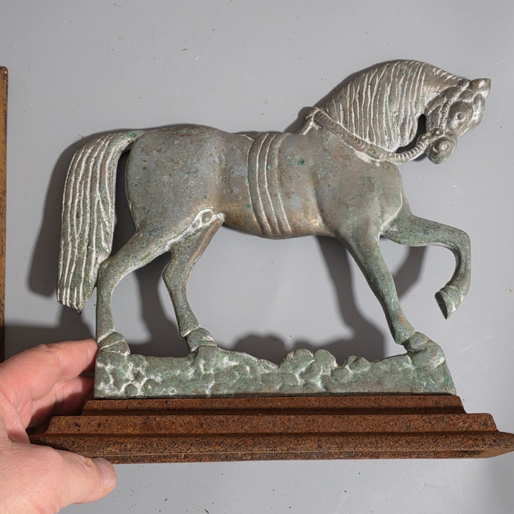 A pair of 19th-century cast iron and brass doorstops featuring prancing horses mounted on stepped rectangular bases with aged patina. View III