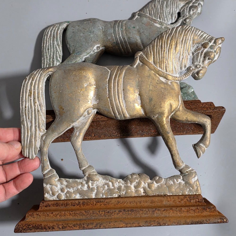 A pair of 19th-century cast iron and brass doorstops featuring prancing horses mounted on stepped rectangular bases with aged patina. View IV