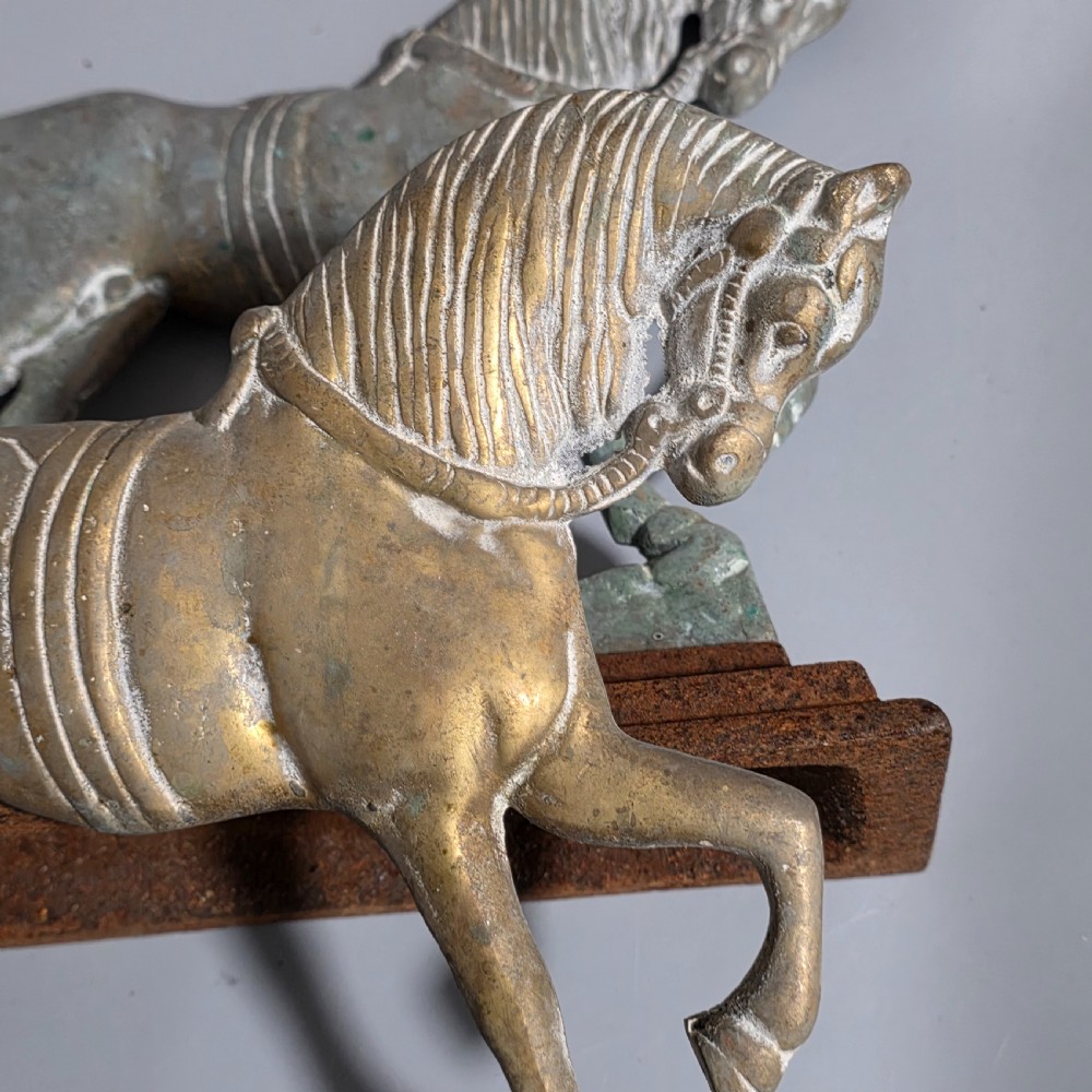 A pair of 19th-century cast iron and brass doorstops featuring prancing horses mounted on stepped rectangular bases with aged patina. View V