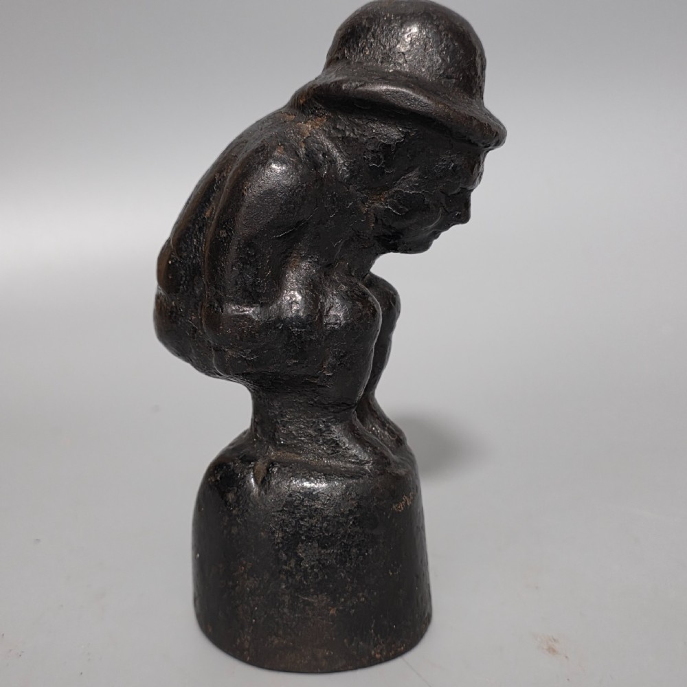 A nineteenth-century dark cast iron paperweight shaped as a crouching male figure in a hat set upon a cylindrical pedestal.